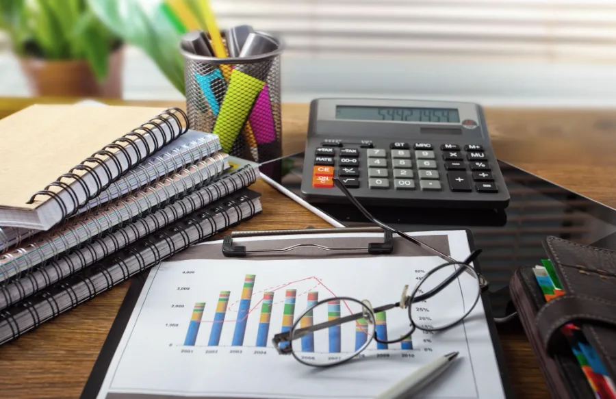 Accounting desk — calculator, printed charts, notebooks and reading glasses